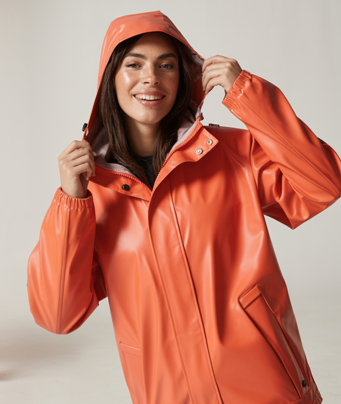 A model wearing vibrant, stylish rainwear — including a waterproof jacket, boots, and optional umbrella — in a studio setting. The model poses confidently with natural movement, evoking protection, comfort, and playfulness in wet weather. Lighting reflects the slight sheen of the waterproof material. Expressions are fresh and upbeat, suggesting readiness for rain with a fashionable edge. Include dynamic poses such as mid-step, holding the hood, or playfully using the umbrella.