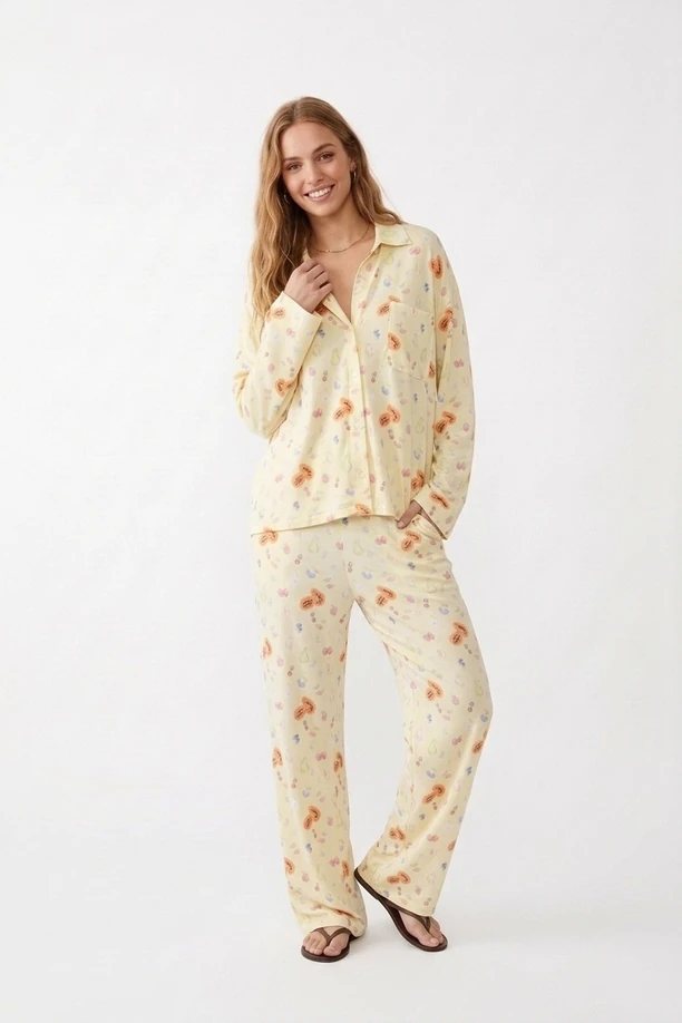 Model in pale butter yellow fruit-print loungewear pajama set with button-down shirt and wide-leg trousers.