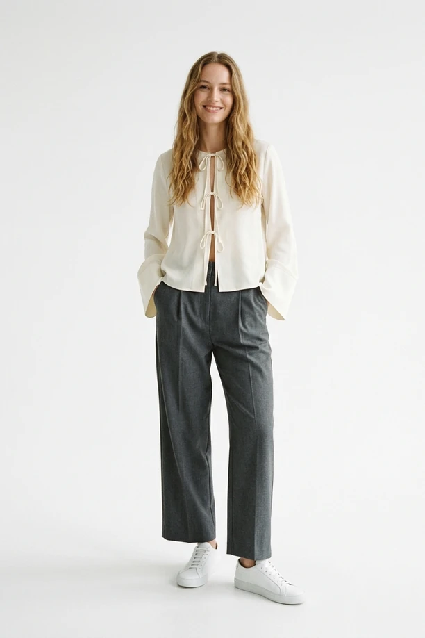 Mannequin en blouse fluide écru à nouettes et pantalon large plissé gris anthracite.