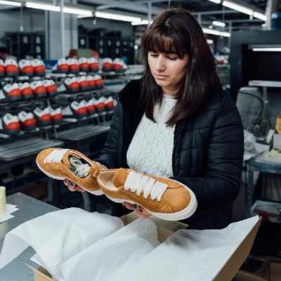Portugal Shoes worker doing the quality control of two orange sneakers.