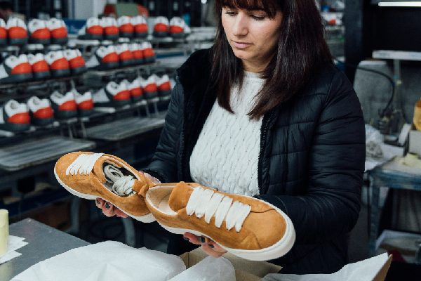 Portugal Shoes worker doing the quality control of two orange sneakers.